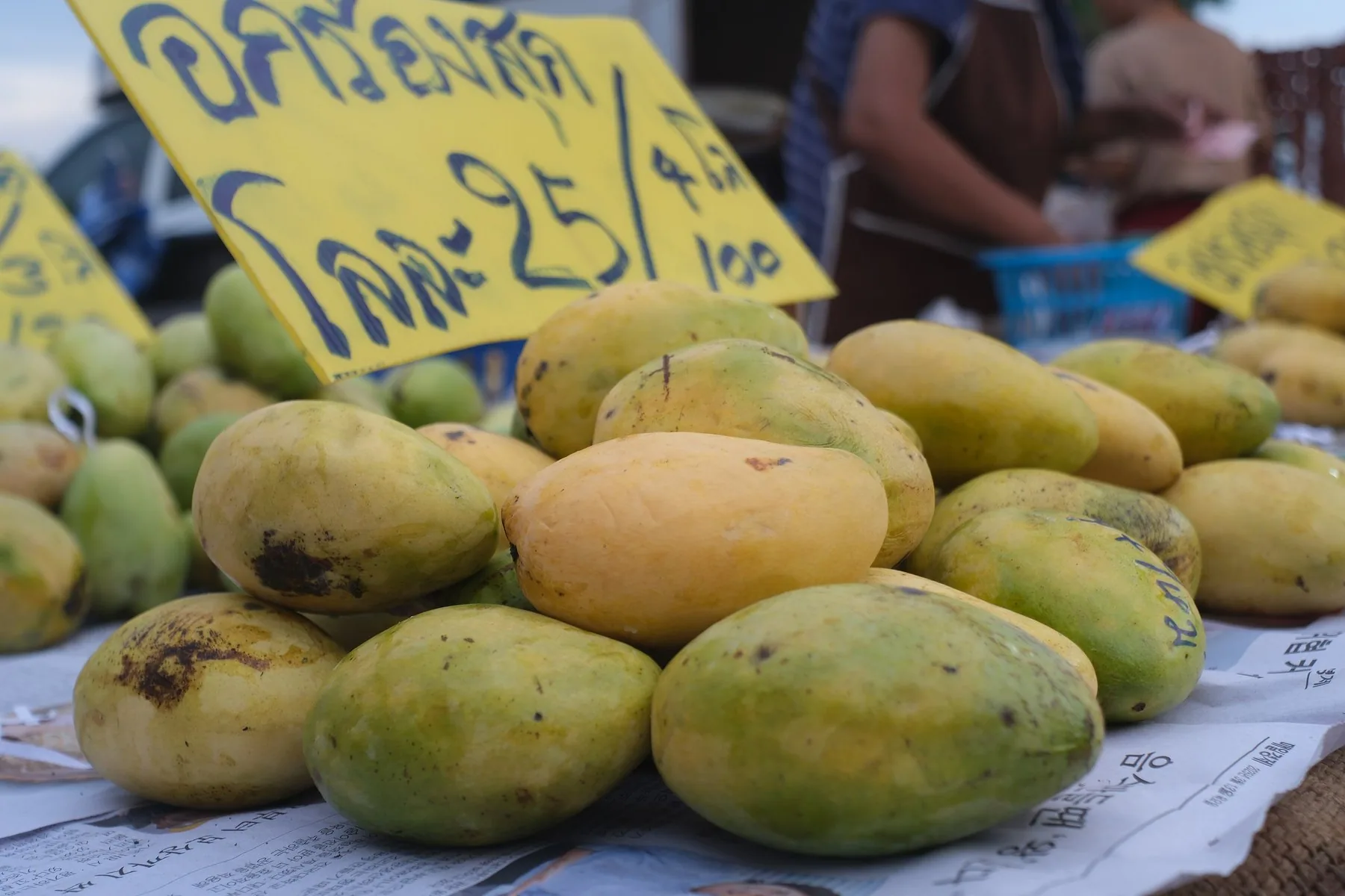 Mango i en bunke foran et gult, håndskrevet prisskilt på et marked