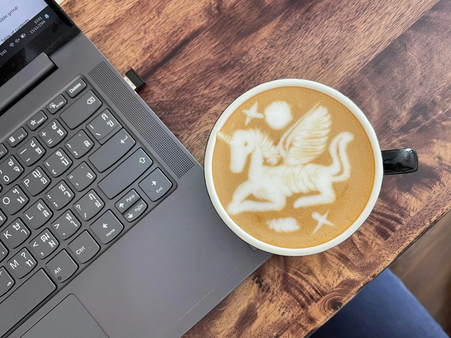 Bærbar PC og en kopp cappuccino med latte art på et trebord