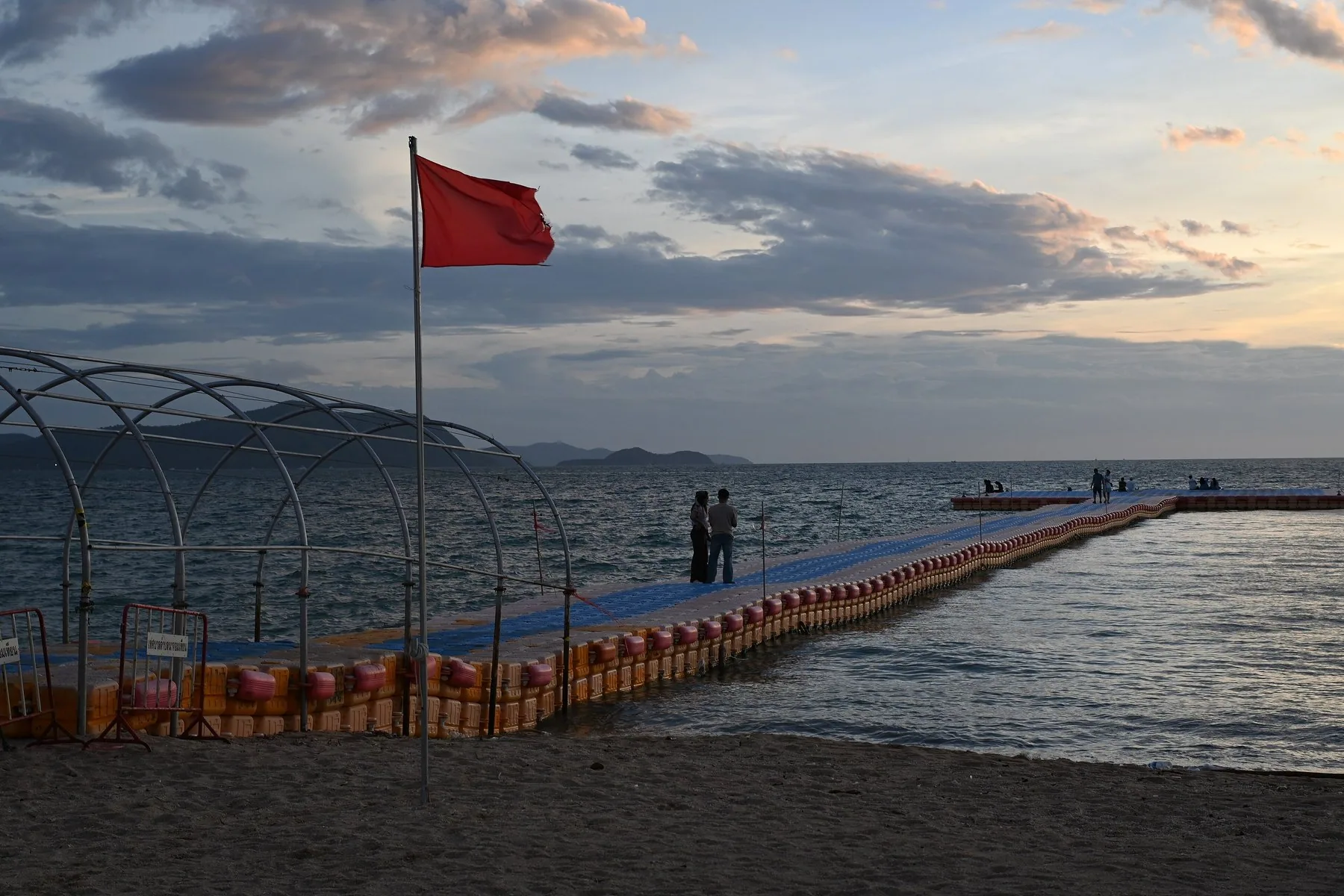 Röd flagga vid en flytbrygga på Na Chom Thian-stranden i skymningen