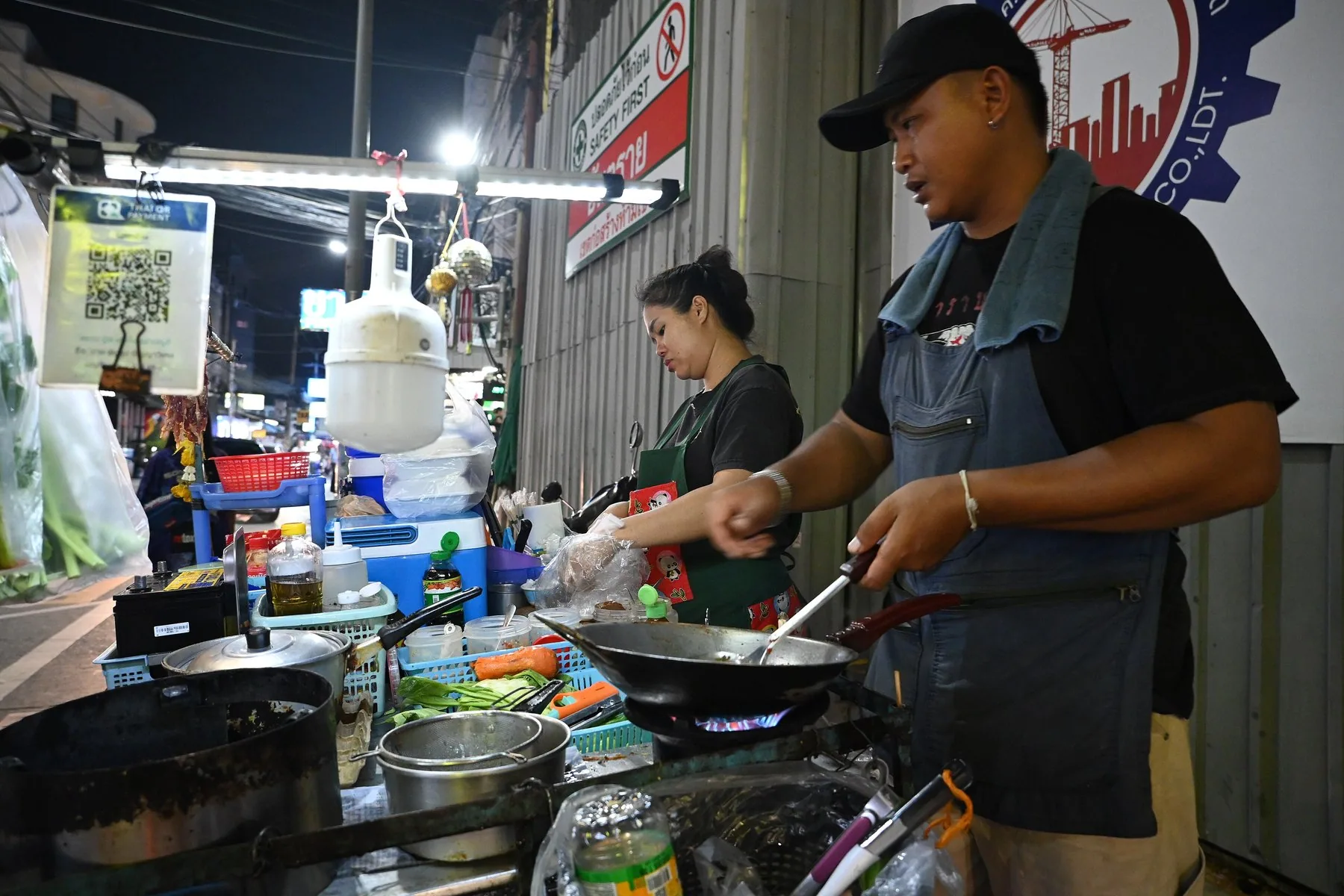 Gatukockar steker i wok vid ett matstånd på nattmarknaden i Nong Pla Lai i Pattaya
