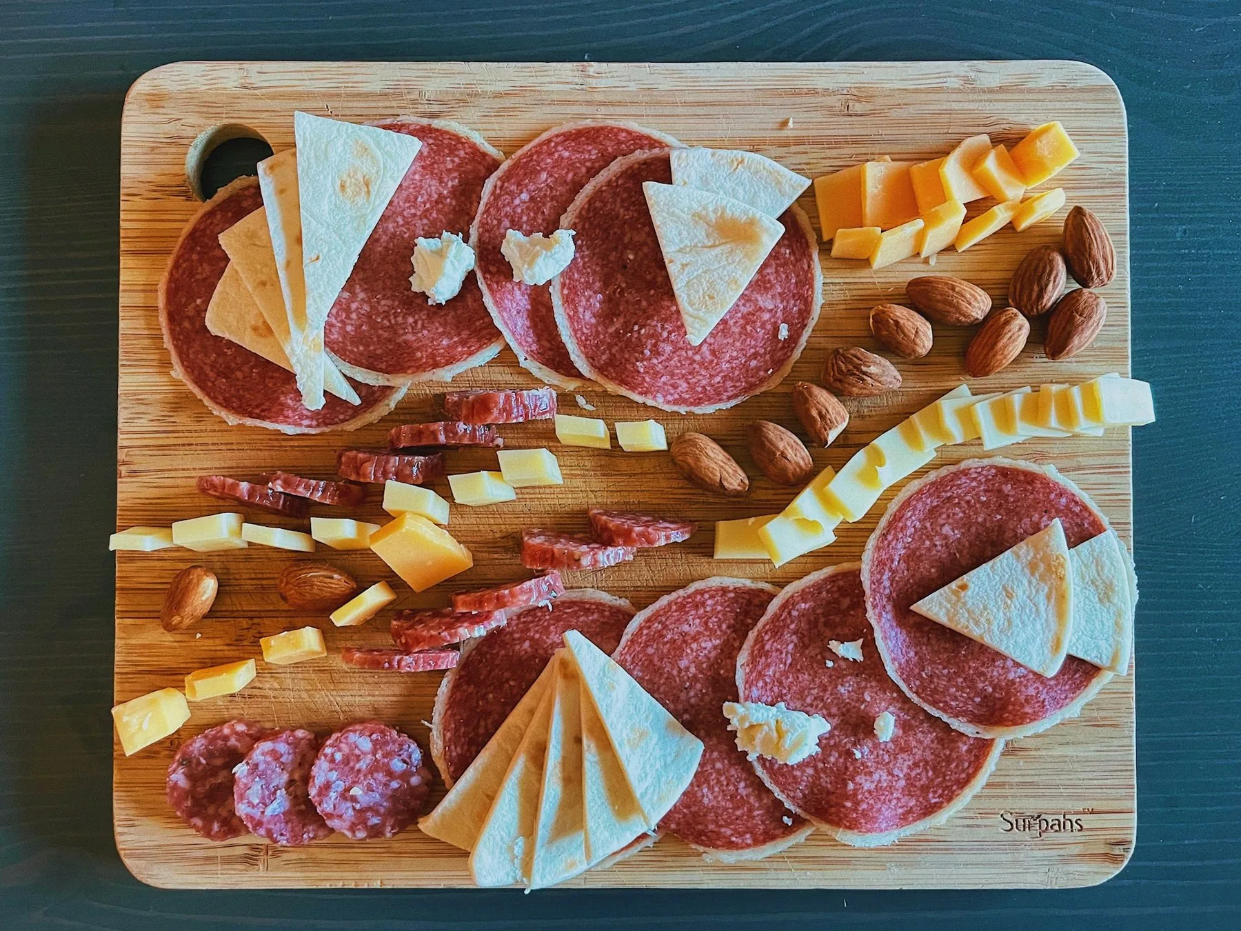 Bræt med salami, hvid ost og mandler set ovenfra
