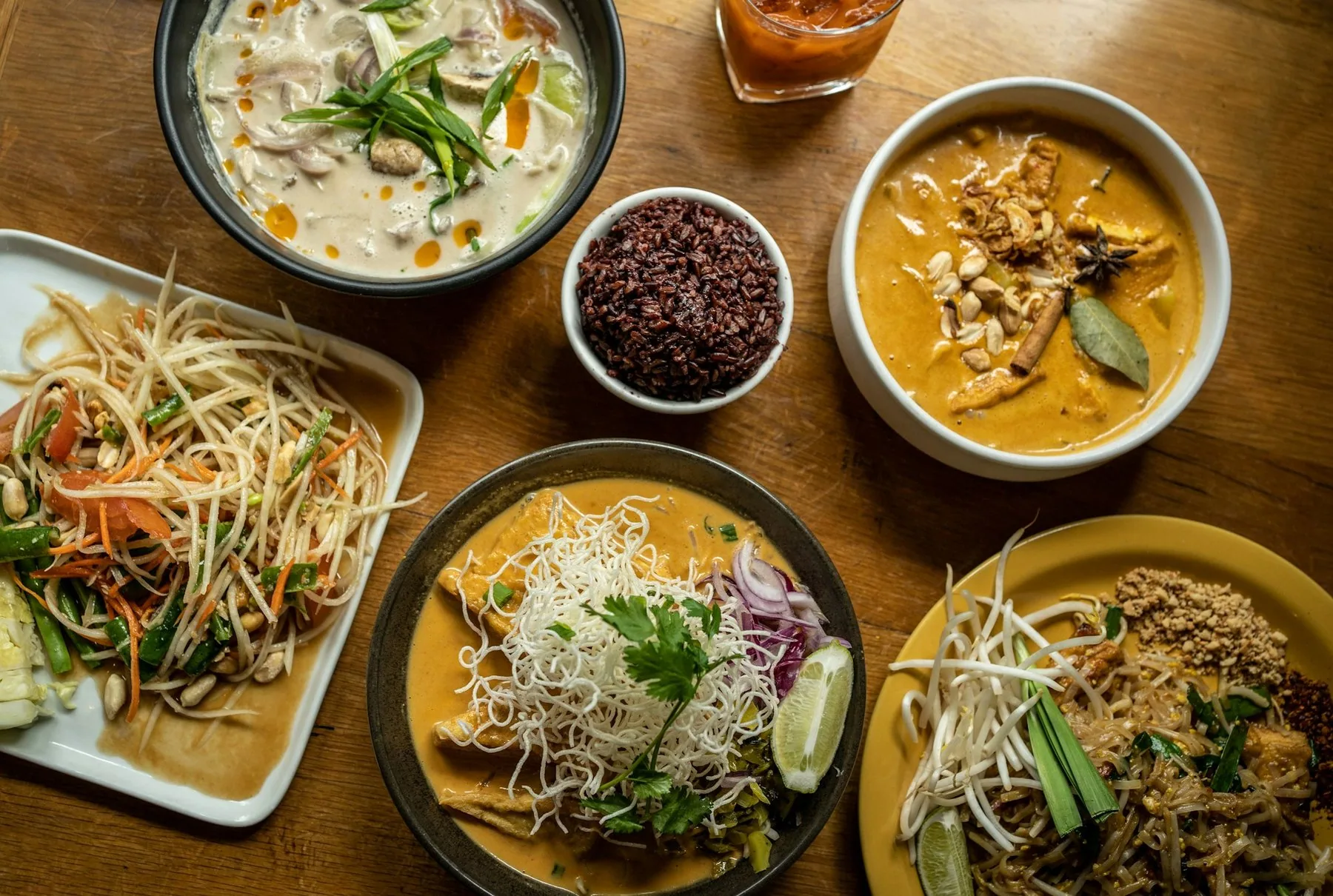 Bord med thailändska rätter: papayasallad, curry, nudlar och ris