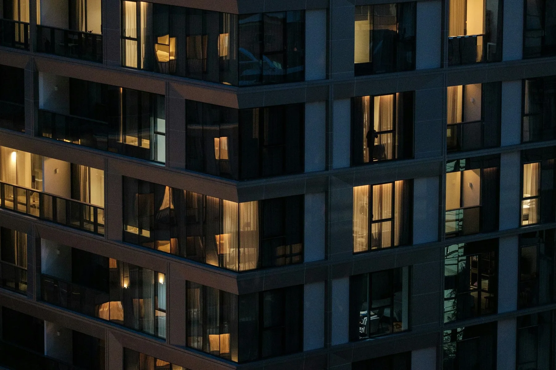 Modernt bostadshus med balkonger och upplysta fönster i kvällsmörkret