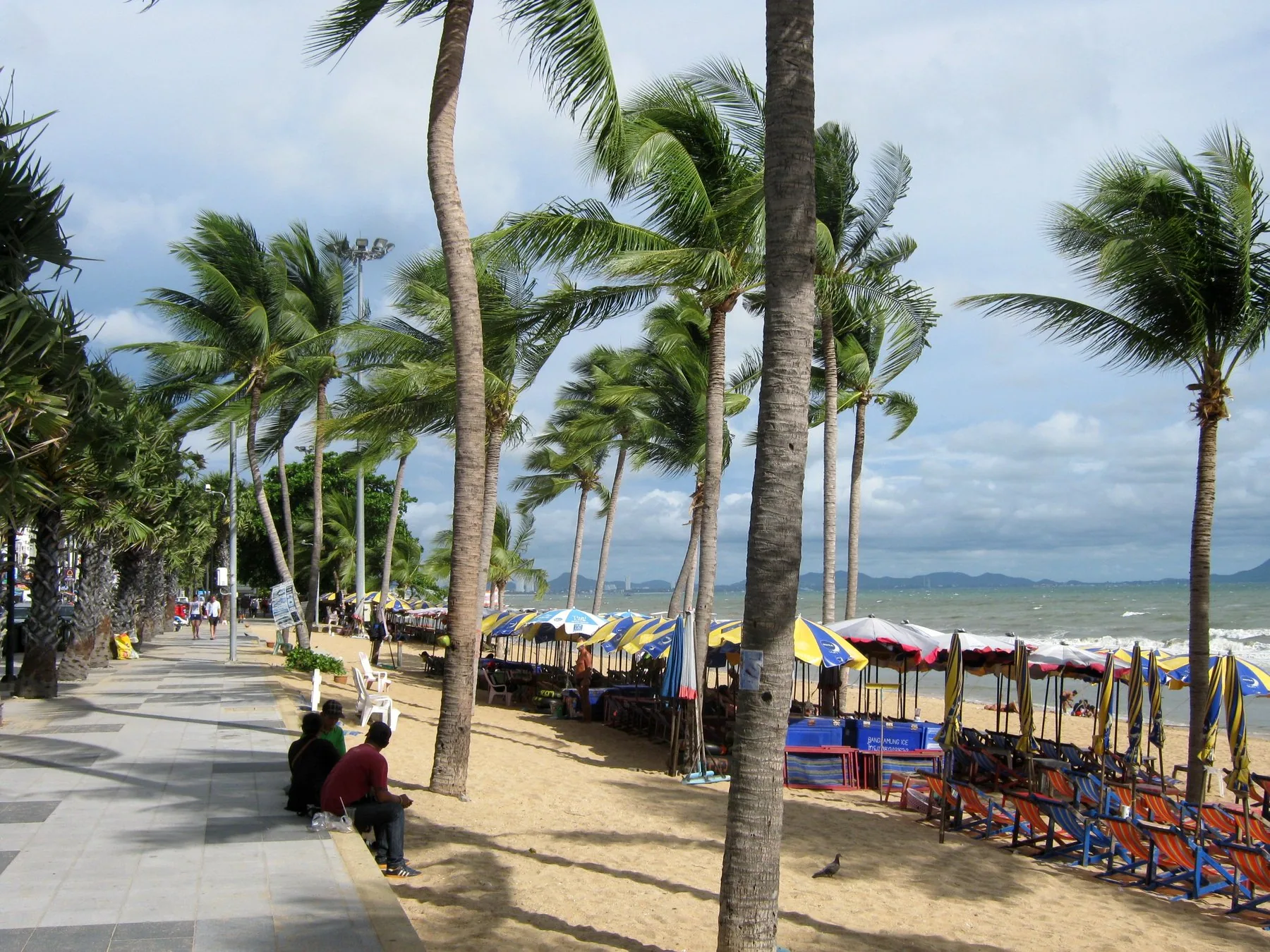 Strandpromenaden ved Jomtien Beach med palmer, parasoller og liggestole en blæsende dag