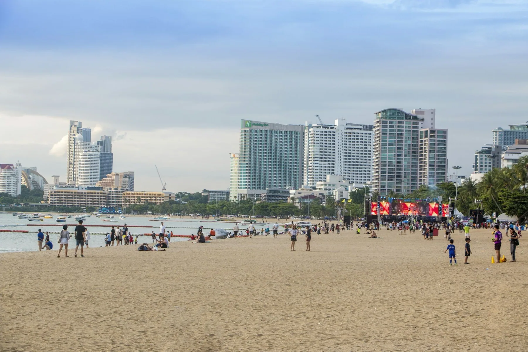 Pattaya Beach med badegjester på sanden og hotelltårn langs Beach Road i bakgrunnen