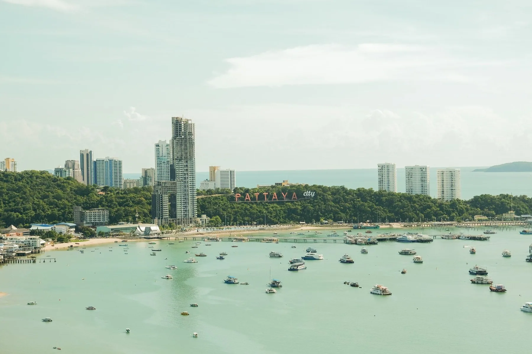 Den skogklädda Pratumnak-höjden med Pattaya-skylten, höghus och båtar för ankar i bukten