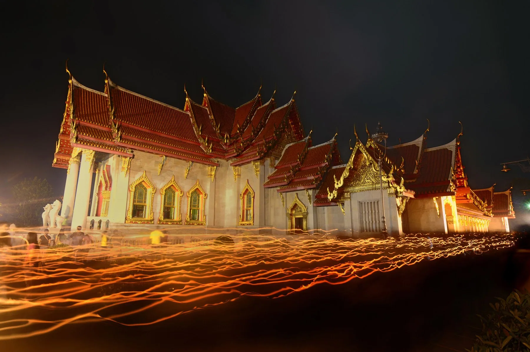 Buddhistisk klosterbygning oplyst om aftenen med lysprocession på en helligdag