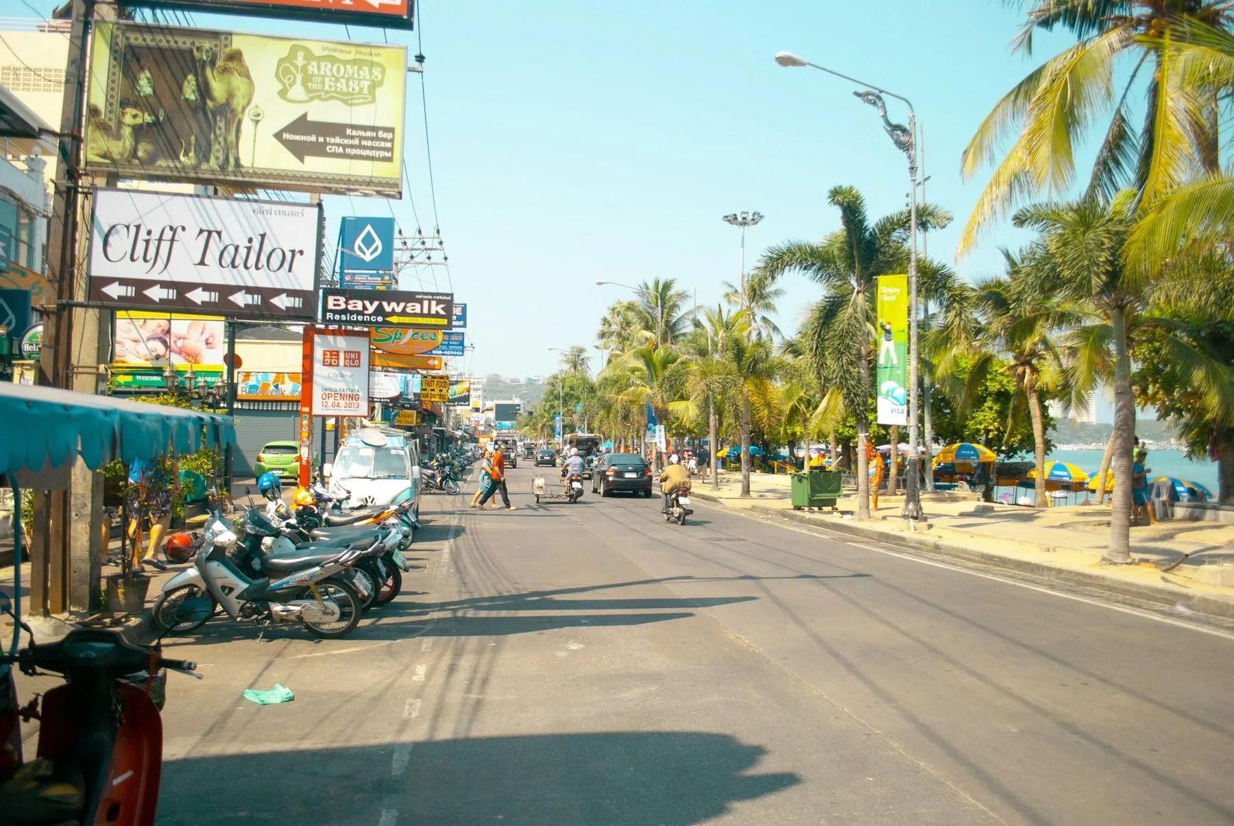 Gata med skräddarskylt, butiker och palmer längs strandvägen i Pattaya
