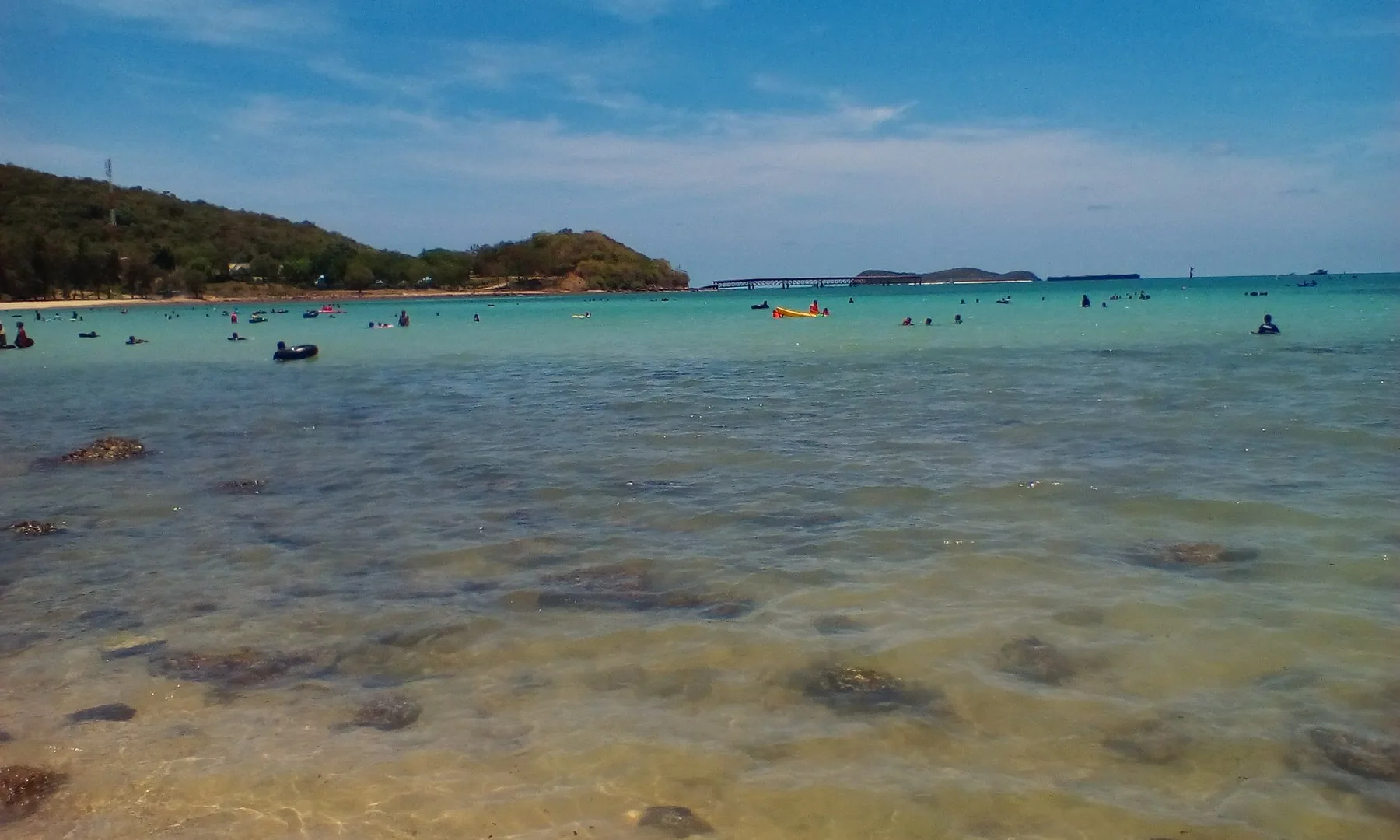 Klart, grunt vann og badende ved en strand i Sattahip-distriktet
