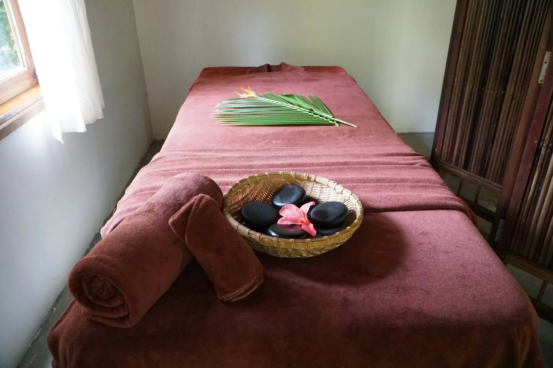 Massasjebenk med håndkle og en kurv med varme steiner og blomst i et spa