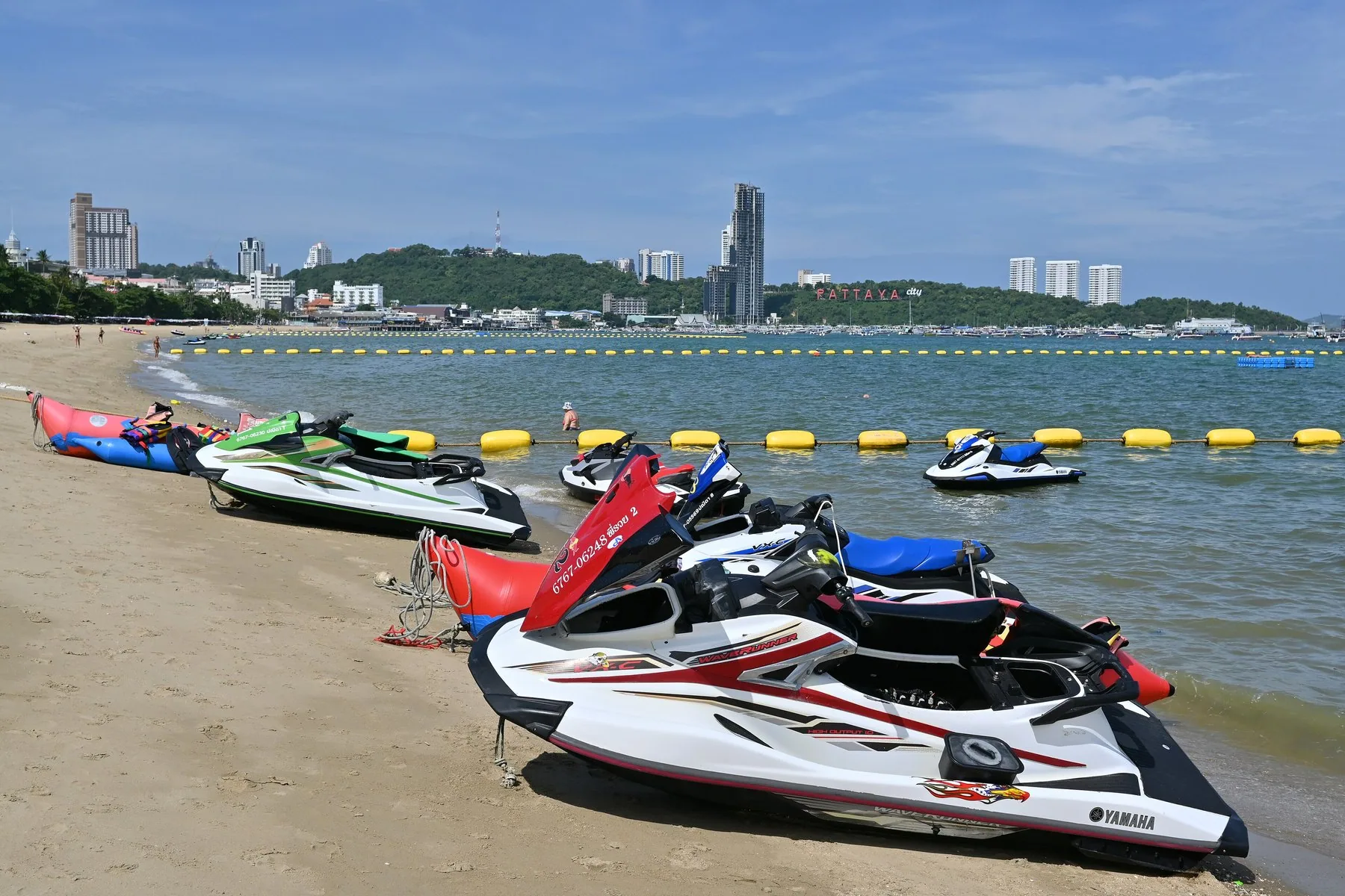 Jetski trukket op på Pattaya Beach med bøjer og byens skyline i baggrunden
