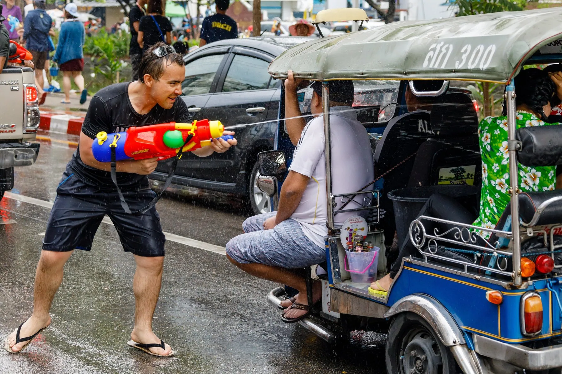 Mand med vandpistol sigter mod en tuk-tuk under Songkran-fejringen