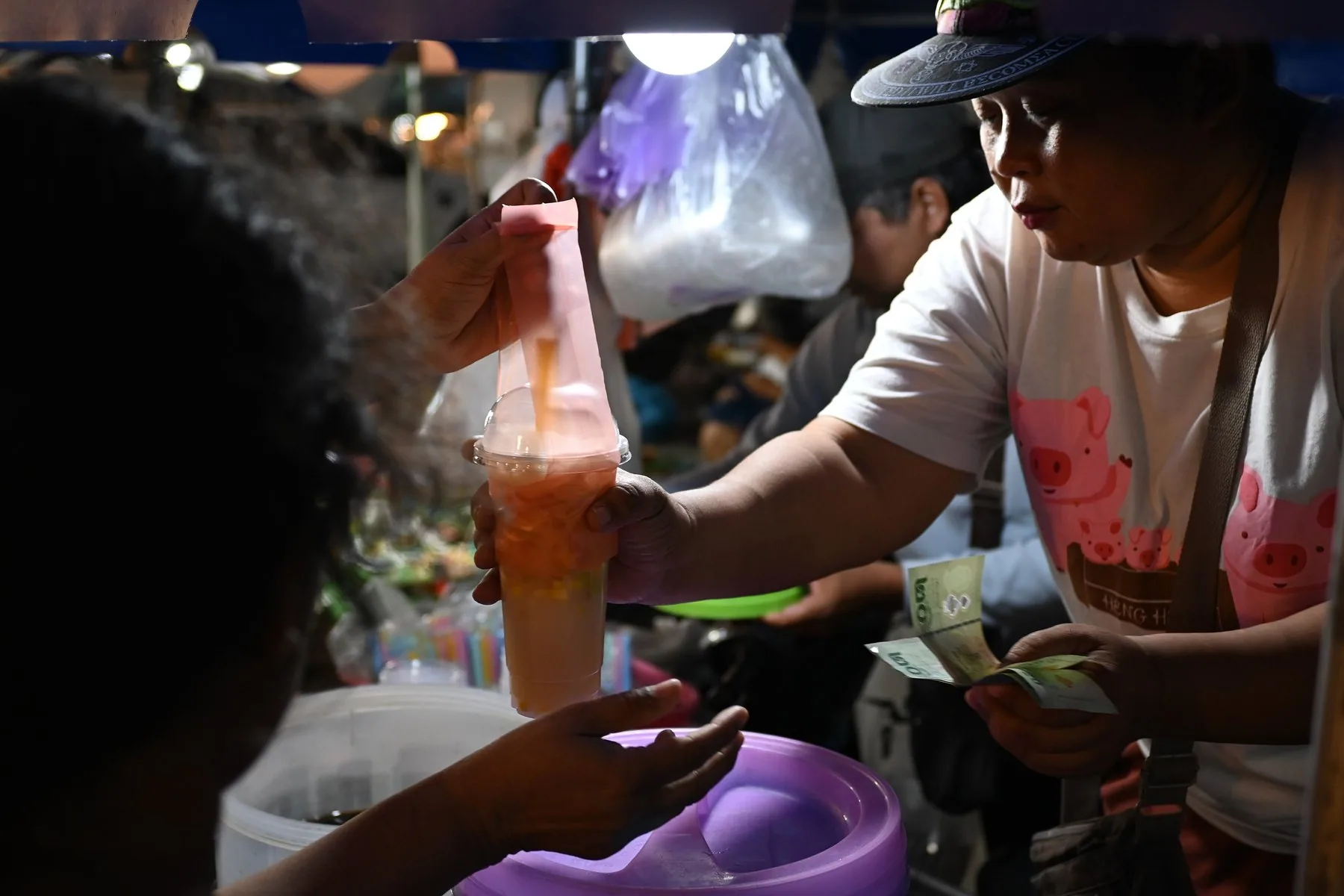 Kunde betaler med thailandske sedler for en iskald drink på et nattmarked