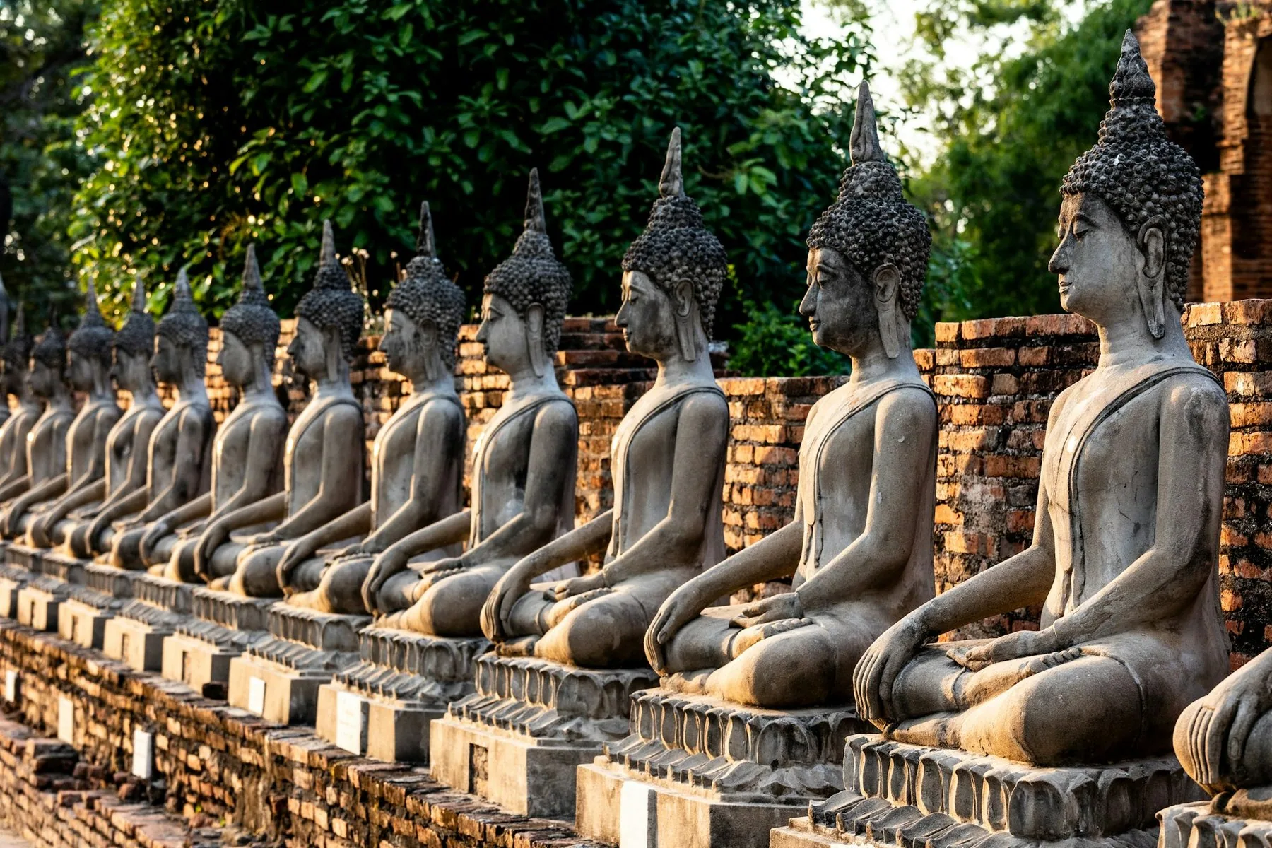 En lång rad Buddhastatyer i sten framför gamla tegelmurar i Ayutthaya