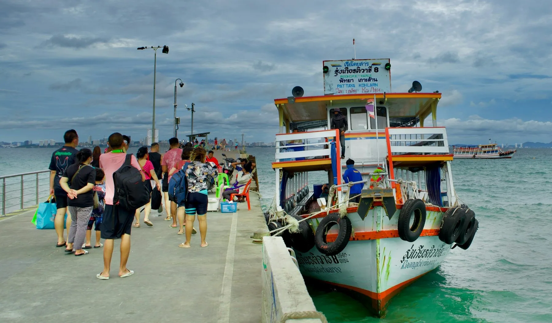 Passasjerer går om bord i en øyferje ved brygga i Pattaya en overskyet dag