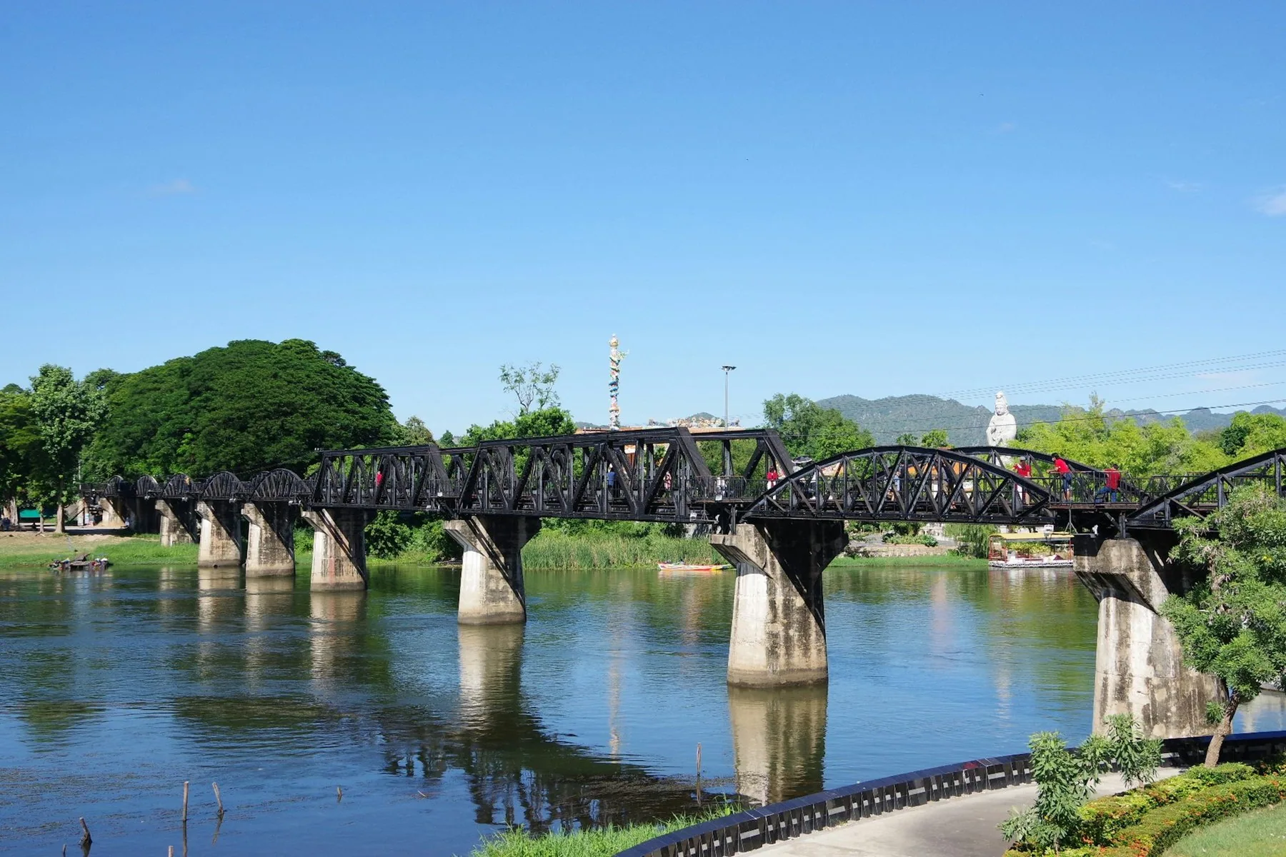 Järnvägsbron över River Kwai i Kanchanaburi med gröna träd och blå himmel