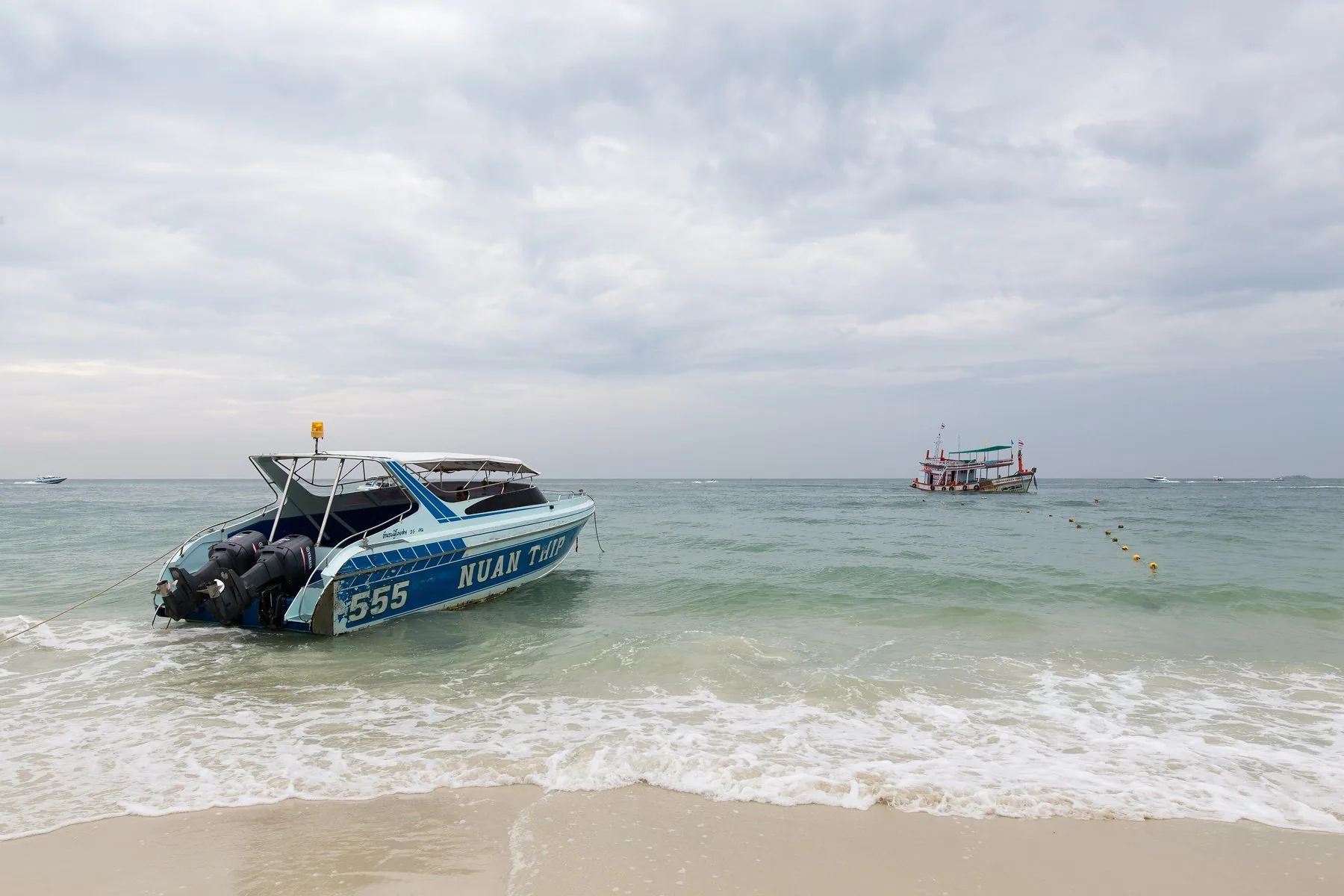 Speedbåt for anker i grunt, klart vann ved en strand på Koh Samet